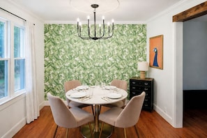A dining room with a round table, chairs, a chandelier, a wall with leaf-pattern wallpaper, a cabinet, and a window with curtains. - Costy Stay | 8 minutes to Downtown & Broadway | Free Parking (Nashville)