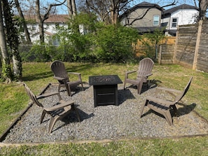 An outdoor seating area with Adirondack chairs and a square table, surrounded by gravel and grass, with houses in the background. - Costy Stay | 8 minutes to Downtown & Broadway | Free Parking (Nashville)