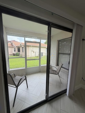 A room with a sliding glass door leading to an outdoor area with a lawn and a house in the background. There are two chairs inside the room. - Modern Kissimmee Retreat Near Disney & Universal (Kissimmee)