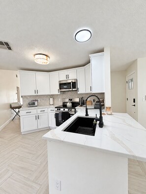A modern kitchen with white cabinetry, stainless steel appliances, and a marble countertop. - Modern Kissimmee Retreat Near Disney & Universal (Kissimmee)