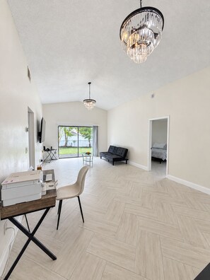 A spacious living area with a large window, a black sofa, a dining table with chairs, and a chandelier. - Modern Kissimmee Retreat Near Disney & Universal (Kissimmee)
