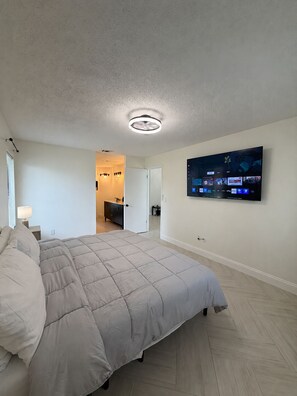 A bedroom with a bed, a television mounted on the wall, and a ceiling light fixture. - Modern Kissimmee Retreat Near Disney & Universal (Kissimmee)