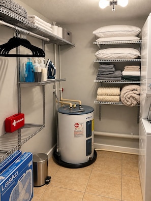 A laundry room with shelves for hanging clothes, a water heater, and storage for linens and cleaning supplies. - The Haus by Lioré 1BD/1BR Near Bucs Stadium & DT (Tampa)