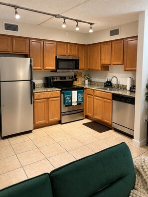 A modern kitchen with wooden cabinets, stainless steel appliances, and a green couch. - The Haus by Lioré 1BD/1BR Near Bucs Stadium & DT (Tampa)
