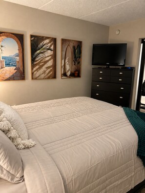 Une chambre à coucher avec un lit, un téléviseur posé sur un meuble et trois tableaux encadrés accrochés au mur.