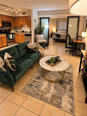 A modern living room with a green sofa, a round coffee table, and a kitchen in the background. - The Haus by Lioré 1BD/1BR Near Bucs Stadium & DT (Tampa)
