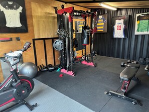 A gym with exercise equipment, a stationary bike, and sports jerseys on the wall. - Country resort -  Have fun with your extended family at this stylish home (Whakamārama)