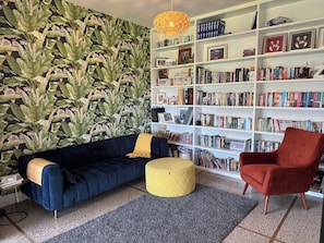 Un saló amb un sofà blau fosc, un otomà groc, una butaca vermella i una estanteria plena de llibres.