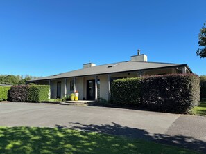 A two-story building with a covered porch, a chimney, and a driveway leading to the entrance. - Country resort -  Have fun with your extended family at this stylish home (Whakamārama)