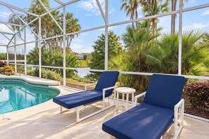 A pool area with lounge chairs and a view of a lake and palm trees. - Lakefront Pool & Theater Near Disney (Kissimmee)