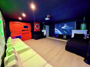 A room with a large flat-screen TV, a red storage unit, and a seating area with white cushions. - Lakefront Pool & Theater Near Disney (Kissimmee)