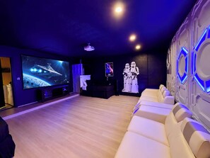 Een bioscoopzaal met een grote flatscreen televisie, een bank en een projector die aan de muur is bevestigd.