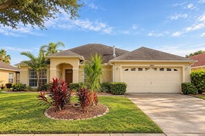 A residential house with a garage, a well-maintained lawn, and a variety of plants. - Lakefront Pool & Theater Near Disney (Kissimmee)