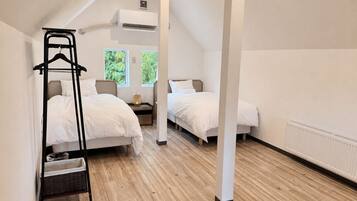 A hotel room with two beds, a wooden floor, a hanging chair, and a window with a view of greenery.