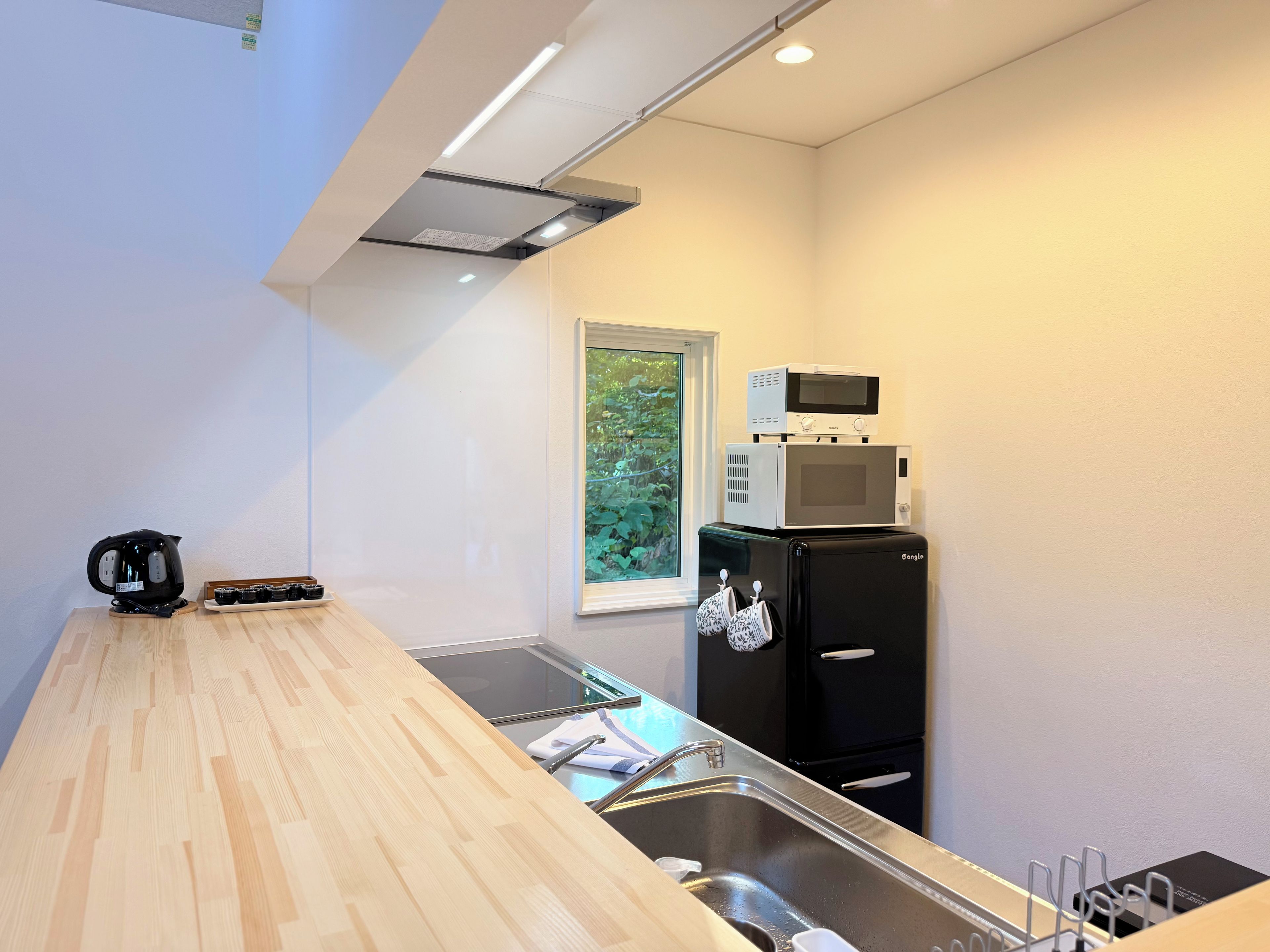 A compact kitchen with a wooden countertop, a black refrigerator, a microwave, and a kettle.
