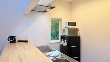 A compact kitchen with a wooden countertop, a black refrigerator, a microwave, and a kettle.