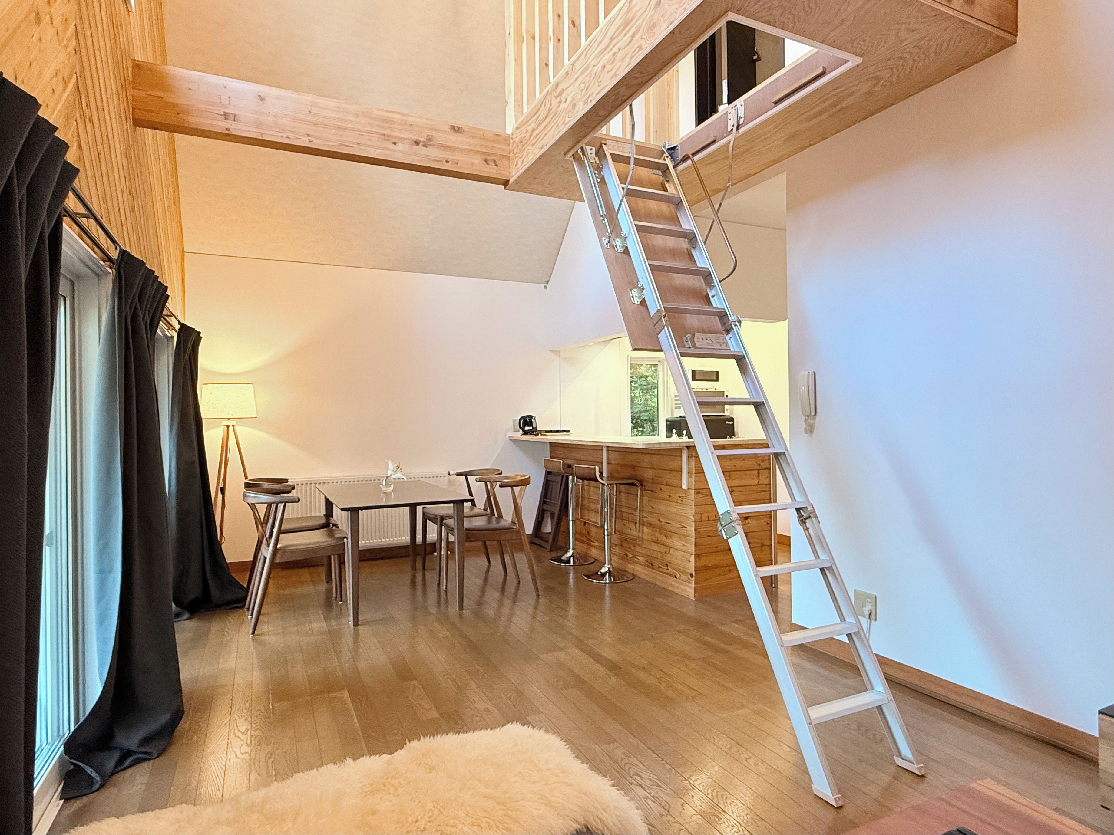 A loft-style room with a wooden staircase, a dining area with a table and chairs, and a kitchen area with a bar.