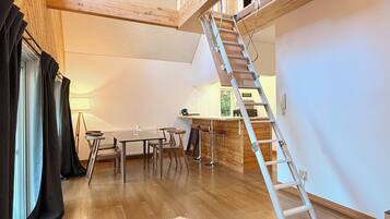 A loft-style room with a wooden staircase, a dining area with a table and chairs, and a kitchen area with a bar.