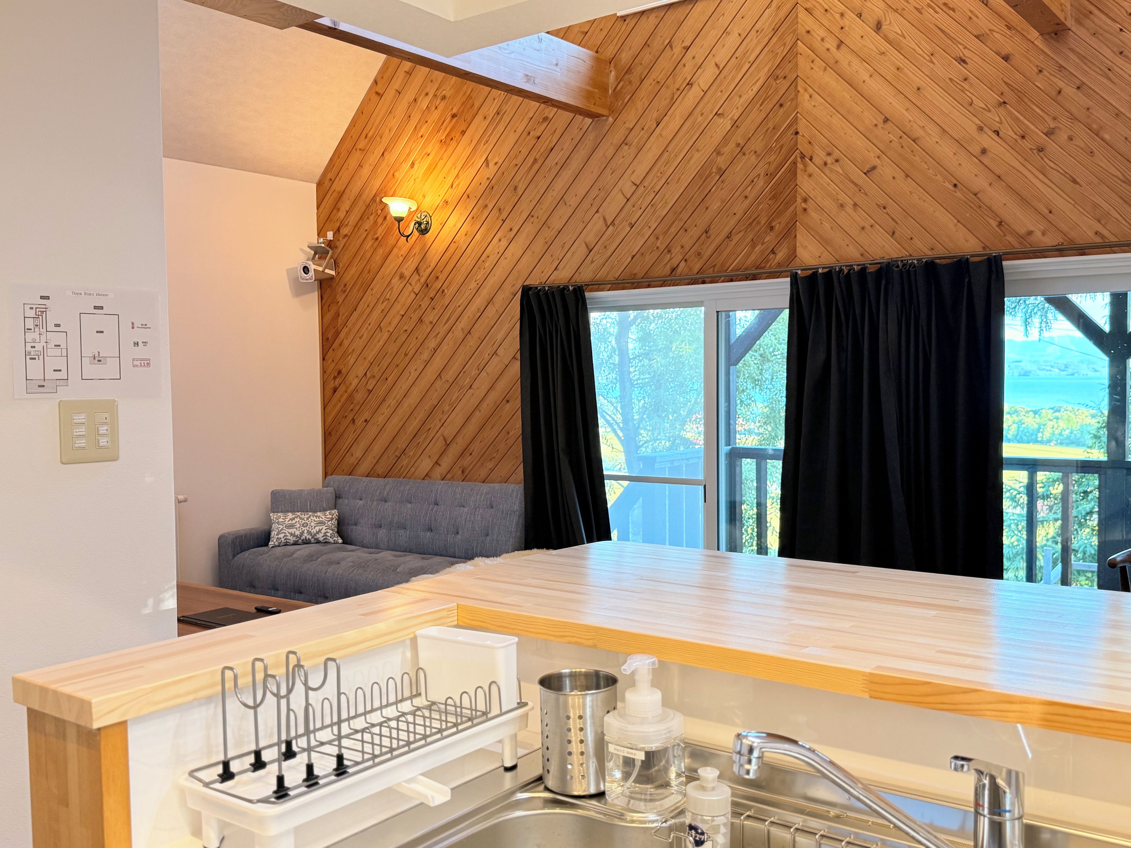 A modern kitchen with a wooden ceiling, a built-in sink, and a window with curtains.