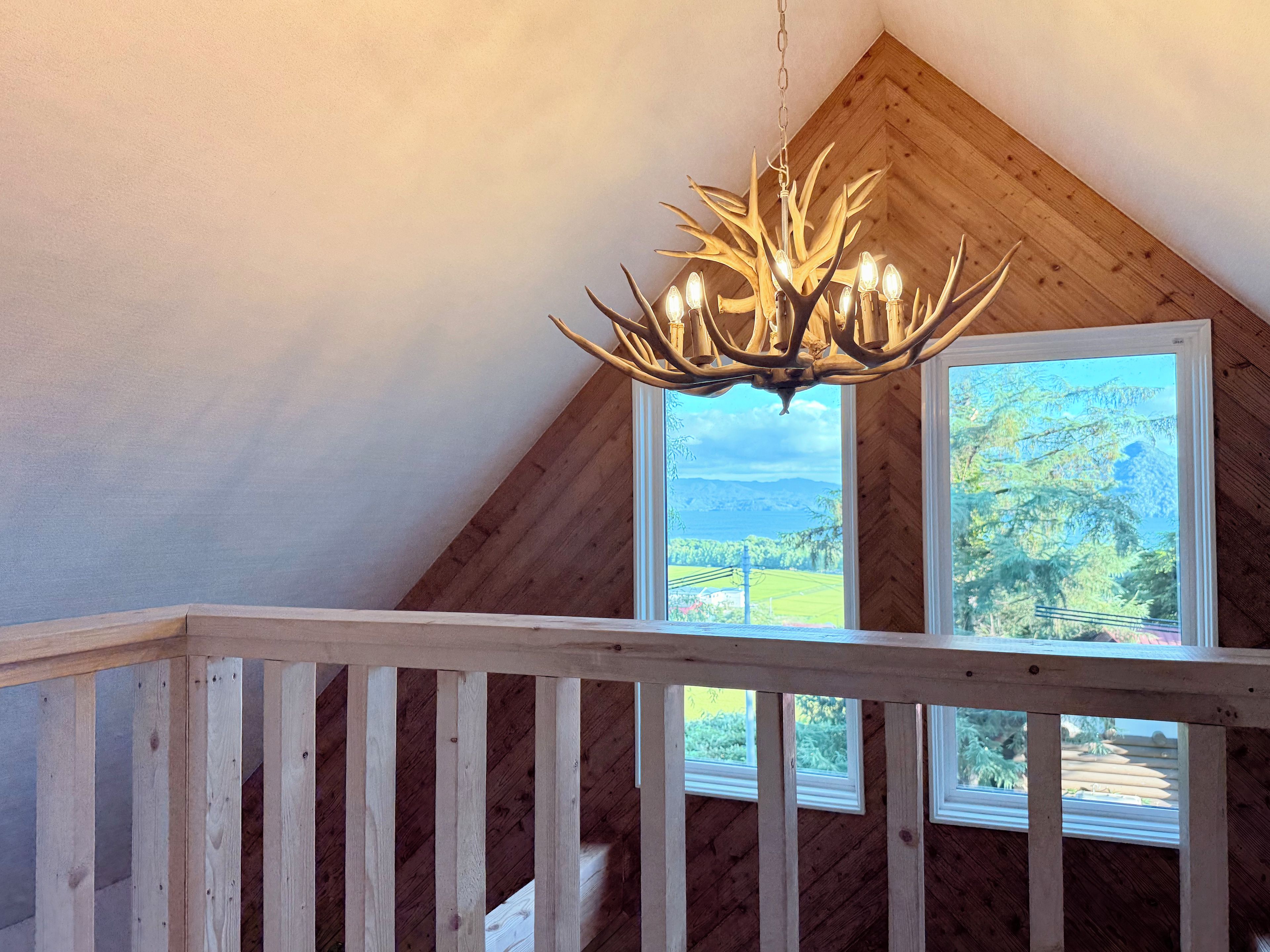 A wooden ceiling with a chandelier and a view of a landscape through a window.