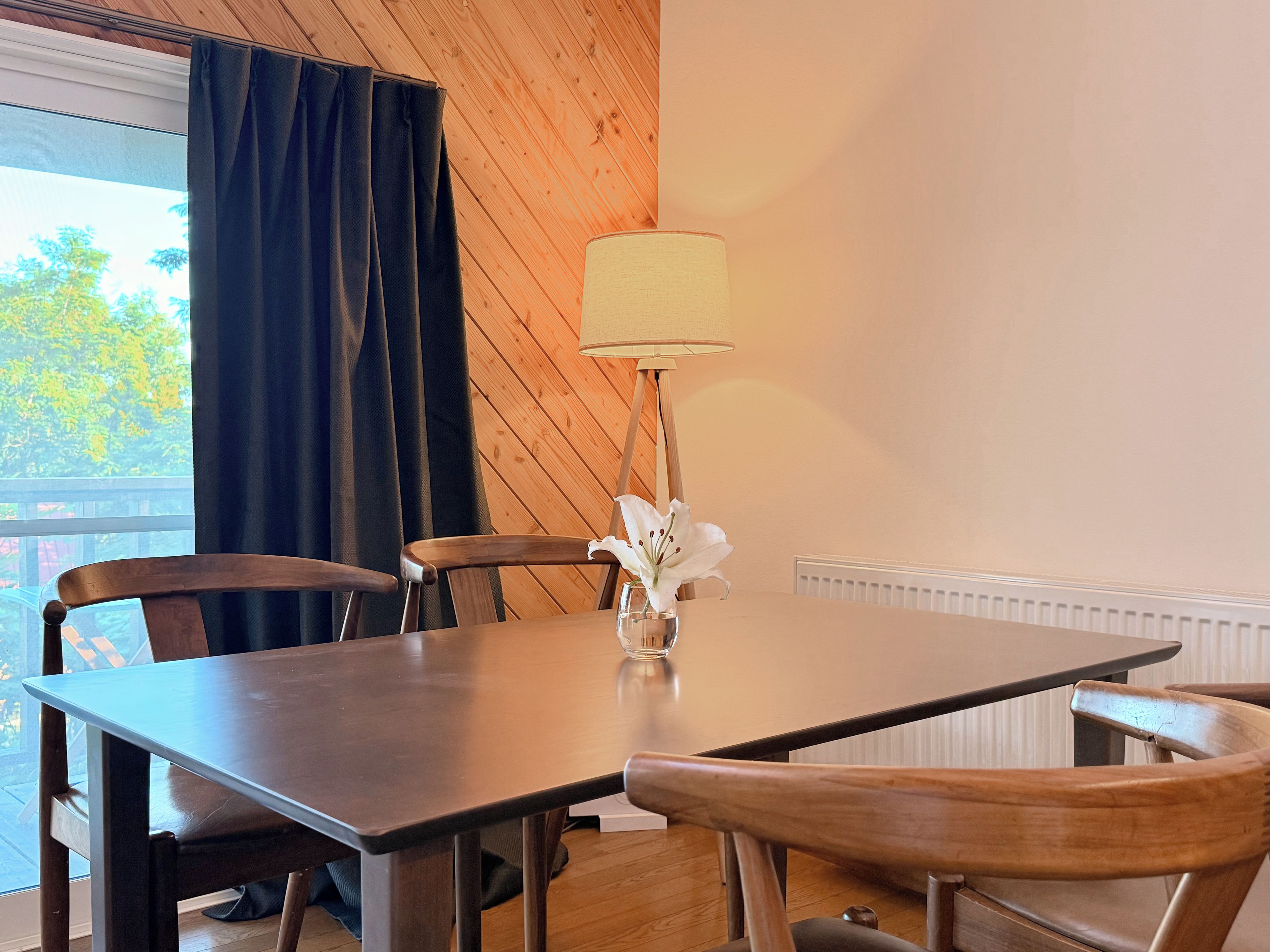 A dining area with a table, chairs, a lamp, and a window with curtains.