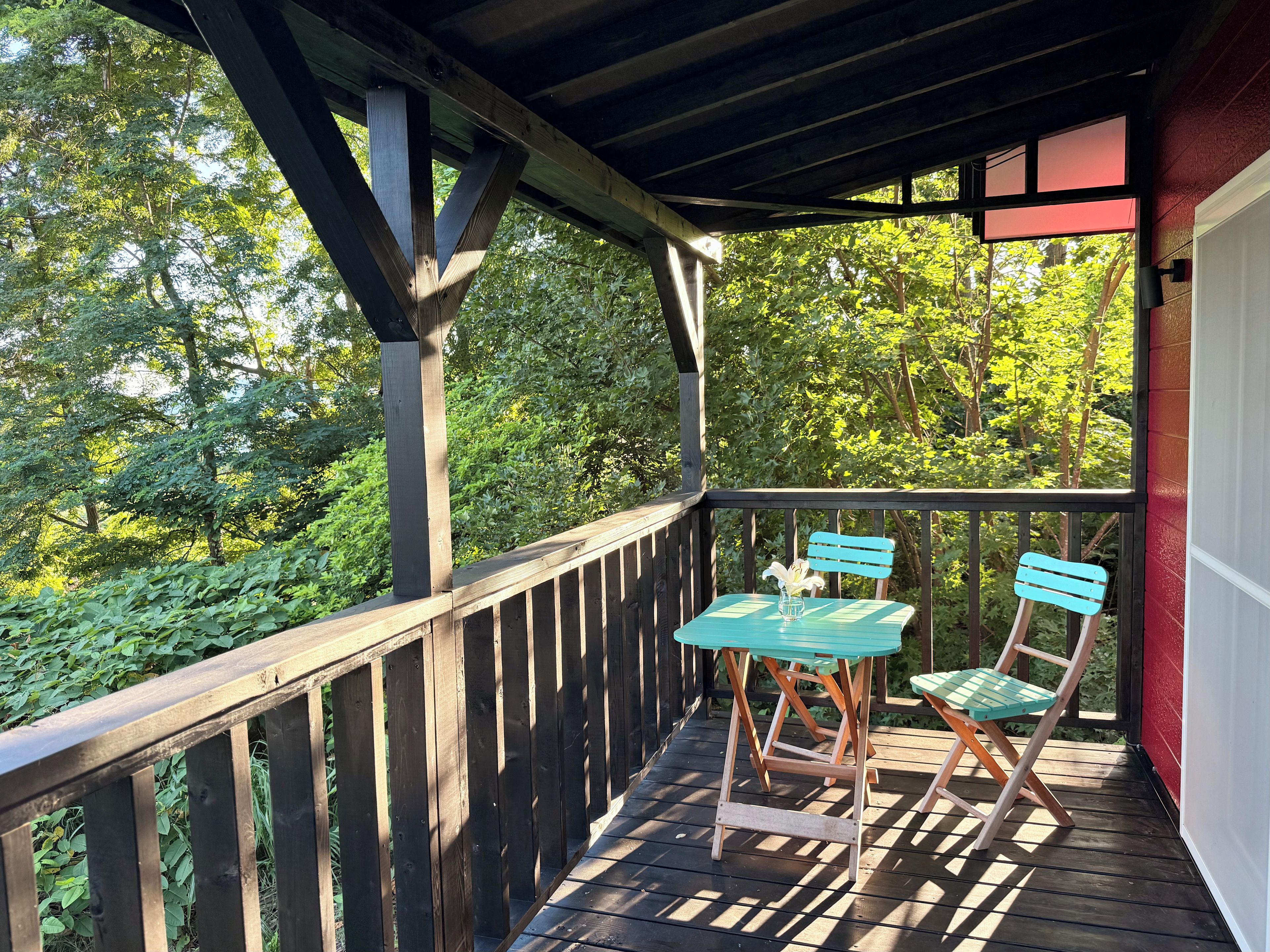 A wooden deck with a table and chairs, surrounded by greenery.