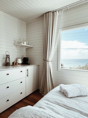 A bedroom with a bed, a nightstand, a window with curtains, and a view of the sea. - Restored Vintage Seaside Home with Pacific Ocean Views (Port Macquarie)