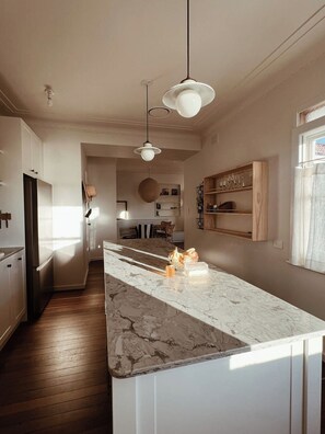 A modern kitchen with a marble countertop, pendant lighting, and wooden shelving. - Restored Vintage Seaside Home with Pacific Ocean Views (Port Macquarie)