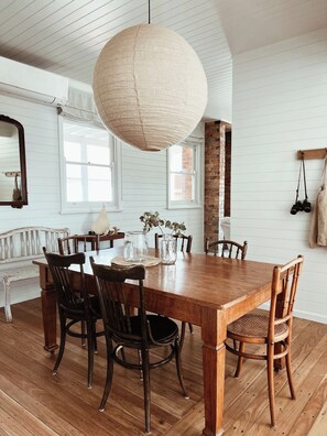 A dining area with a wooden table, chairs, and a hanging light fixture. - Restored Vintage Seaside Home with Pacific Ocean Views (Port Macquarie)