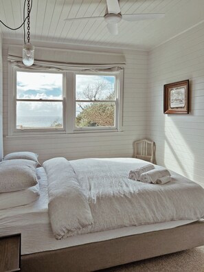 A bedroom with a bed, a window, a ceiling fan, and a framed picture on the wall. - Restored Vintage Seaside Home with Pacific Ocean Views (Port Macquarie)