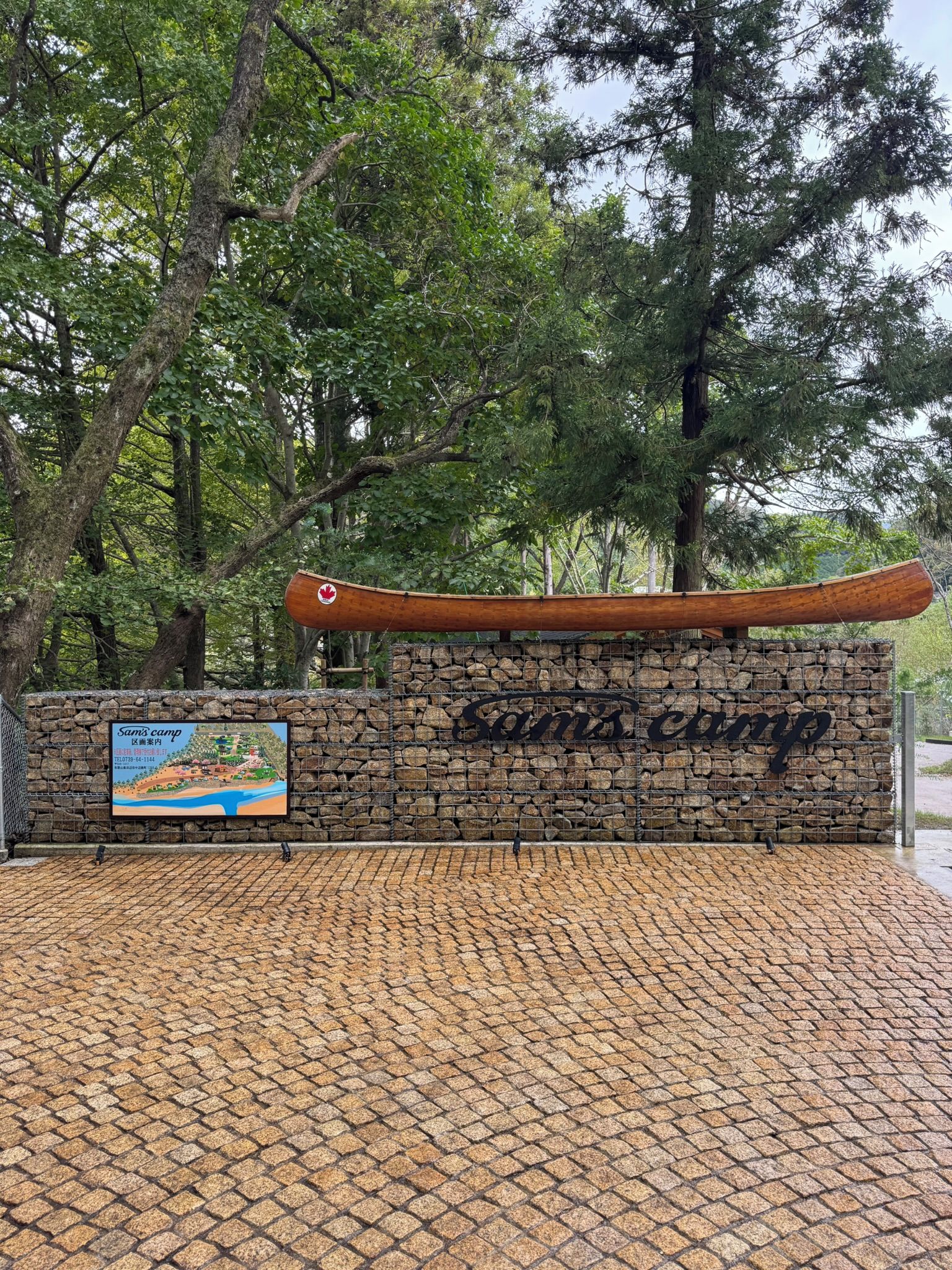 A stone wall with a canoe and a sign for 'Sam's Camp' with a map and contact information.