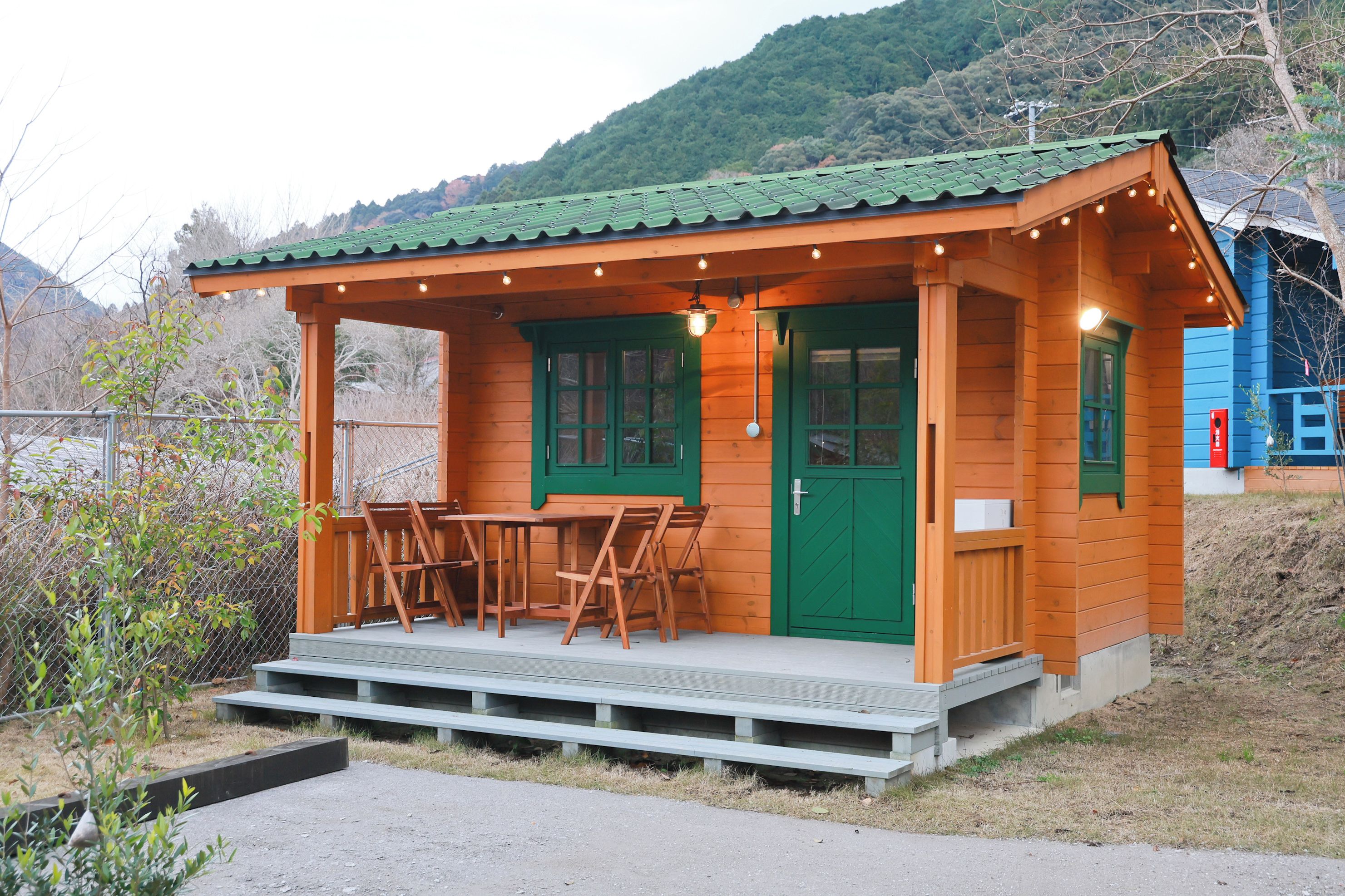 A small wooden cabin with a porch, a green door, and a table with chairs.