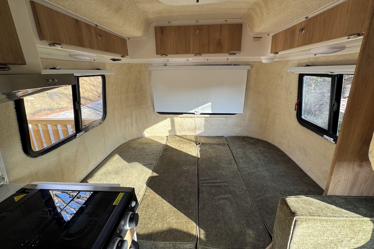 Interior compacto de una caravana con kitchenette, una pizarra y dos ventanas.