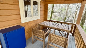 A wooden deck with a table and chairs, a window with blinds, and a blue cabinet.