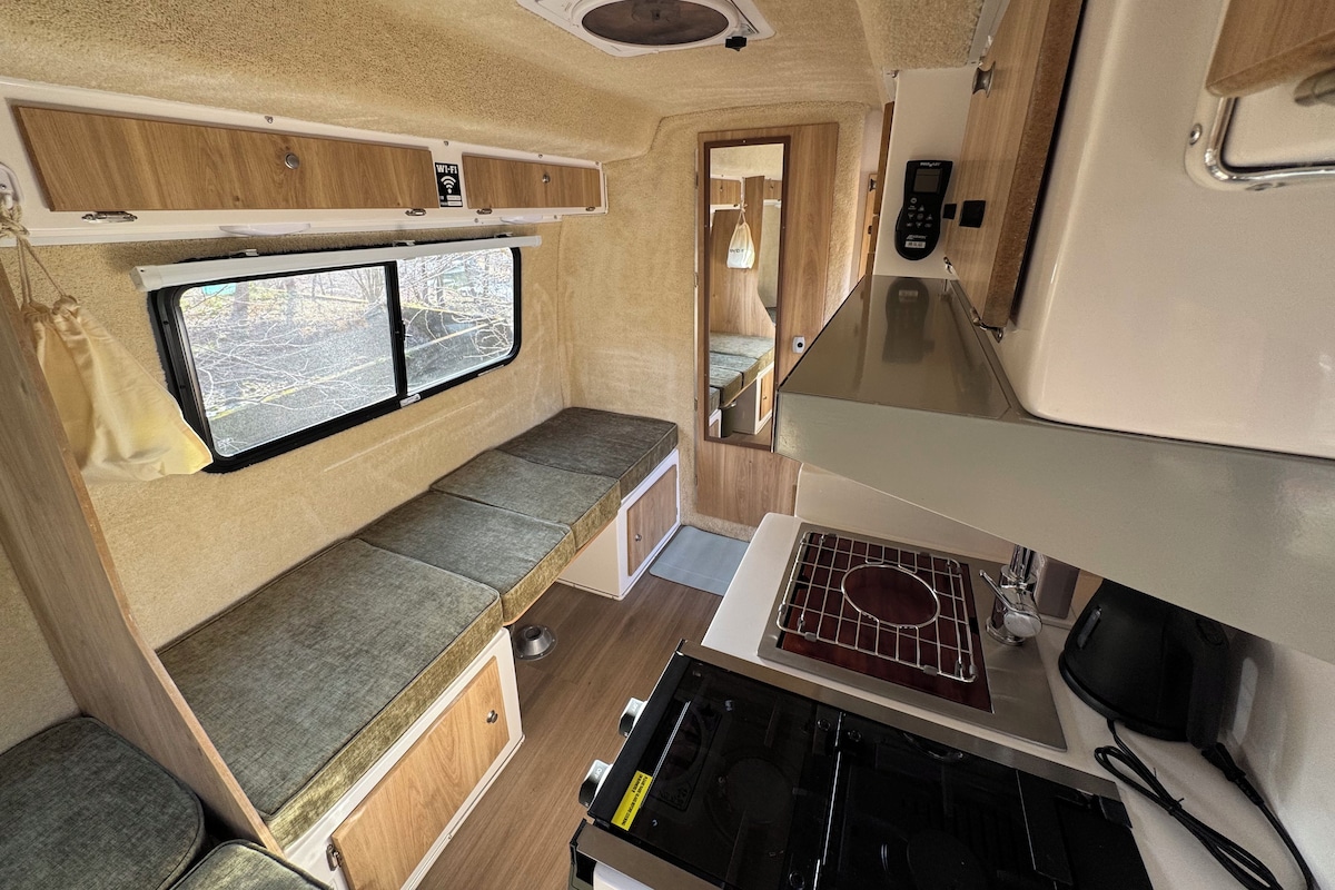 Una kitchenette compacta con estufa, lavamanos y ventana con vistas a árboles.