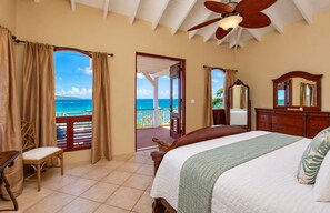A hotel room with a bed, a chair, a wooden dresser, a mirror, and a balcony with a view of the ocean. - Welcome to Villa Amarante , Your East End Caribbean Escape! (Christiansted)