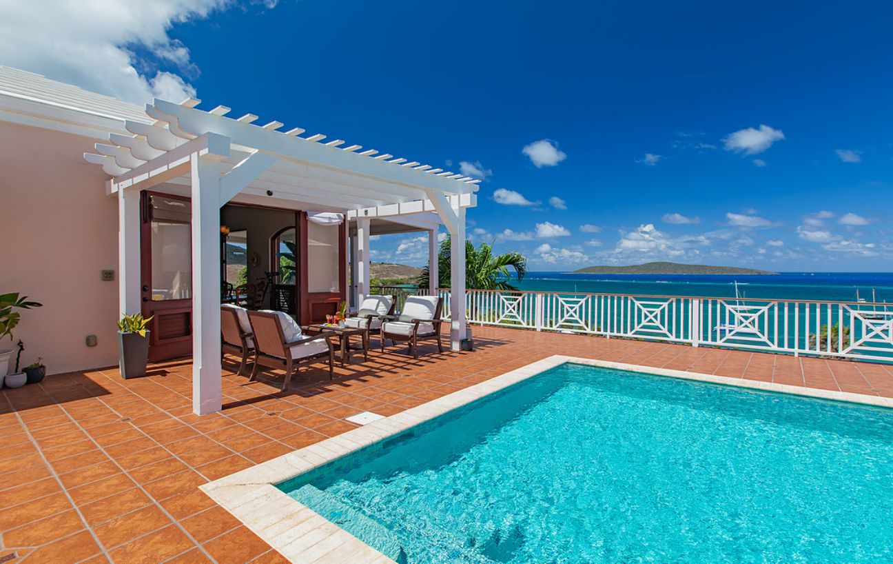 A pool area with a pergola, lounge chairs, and a view of the ocean.