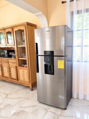 A stainless steel refrigerator with a water dispenser, a wooden cabinet with glass doors, and a marble floor. - Casa del Marino (Tela)