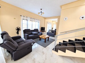 A modern living room with a sofa, a coffee table, and a TV. There is a staircase with a handrail leading to an upper floor. - Casa del Marino (Tela)