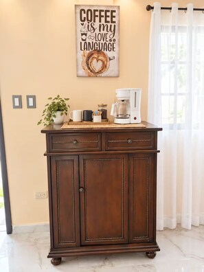 A wooden cabinet with a coffee maker on top, a framed quote on the wall, and a plant beside it. - Casa del Marino (Tela)