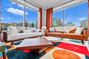 Ein modernes Wohnzimmer mit zwei Sofas, einem Couchtisch und Blick auf die Stadt durch große Fenster.