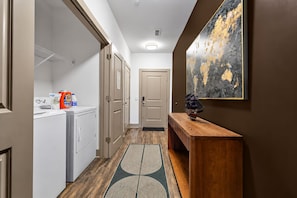 A hallway with a wooden bench, a ship model, and a large abstract painting on the wall. - Mid-century | 5 minutes to Downtown & Broadway |Fitness Gym + Free Parking (Nashville)