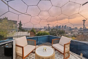 A rooftop terrace with two wicker chairs, a round table, and a view of a city skyline including a distinctive tower. - 2BR Queen Anne Home - Space Needle View + Deck (Seattle)