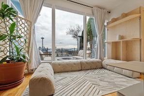 A modern living room with a large window, a potted plant, and a sofa. - 2BR Queen Anne Home - Space Needle View + Deck (Seattle)