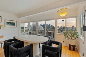 A modern dining area with a round table and chairs, large windows with a city skyline view, and a potted plant. - 2BR Queen Anne Home - Space Needle View + Deck (Seattle)