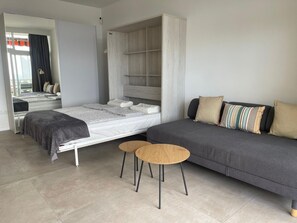 A modern bedroom with a bed, a grey sofa, two small round tables, and a wardrobe. - Studio with a View of the Harbor (Puerto de la Cruz)
