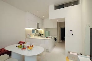 A modern kitchen with white cabinets, a dining area with a table set for four, and a small island with a microwave and toaster.