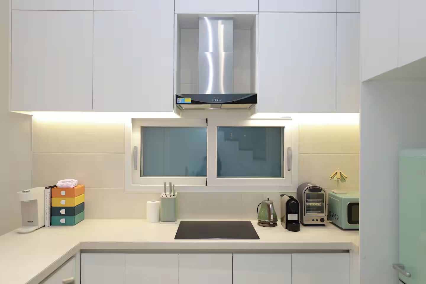 Una cocina moderna con armarios blancos, una campana extractora de acero inoxidable, un ventanal con vidrio esmerilado y un microondas en la encimera.