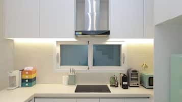 Una cocina moderna con armarios blancos, una campana extractora de acero inoxidable, un ventanal con vidrio esmerilado y un microondas en la encimera.