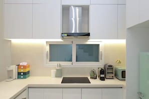 A modern kitchen with white cabinets, a stainless steel range hood, a window with frosted glass, and a microwave on the counter.